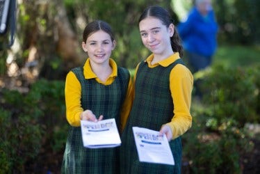 Girl students smiling and handing out information to visitors.