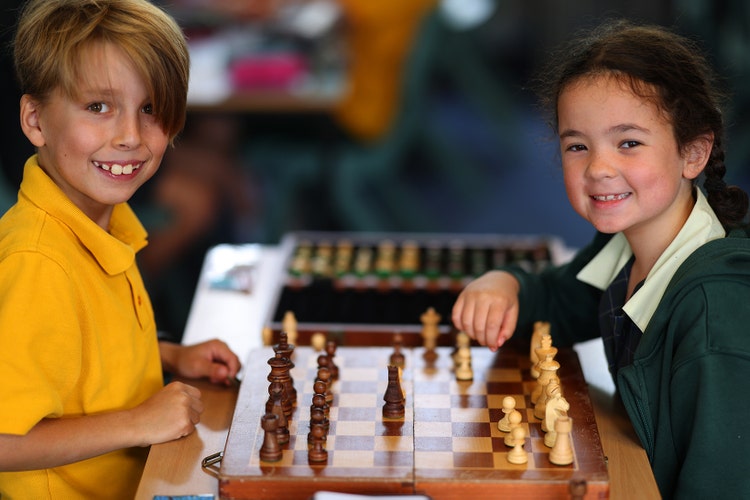 Boy and girl playing chess, smiling at the camera.