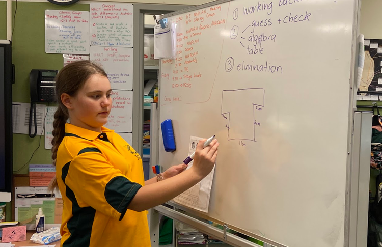 A year 6 student solving a mathematical problem on a whiteboard.