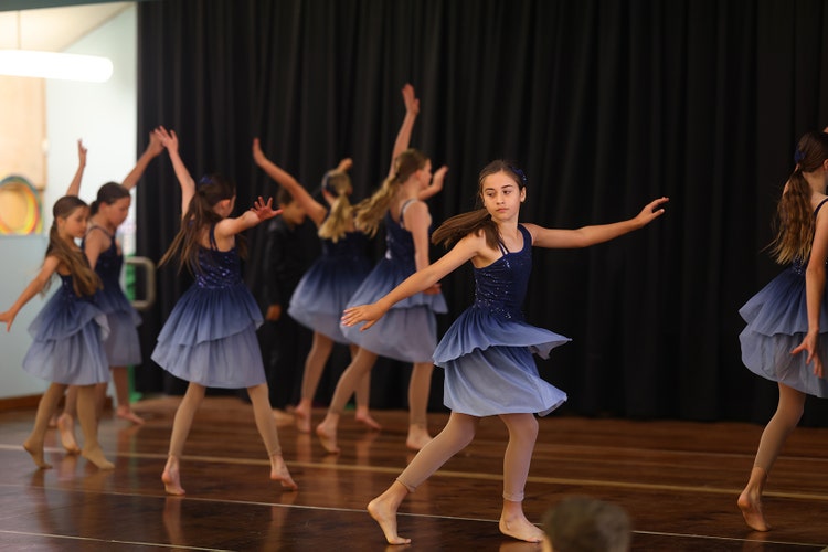 Our dance ensemble performing on stage. The girls are wearing blue dresses with flowing fabric as they dance contemporary style.