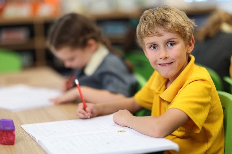 Two students in year 3 completing tasks in exercise books at their desk.