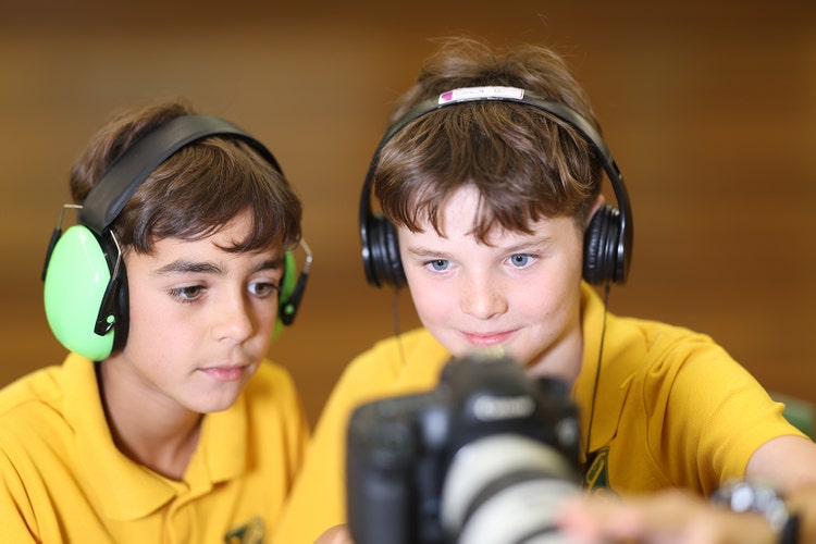 Two boys (students) with headphones on looking back at video footage on a camera. They are part of our media team.