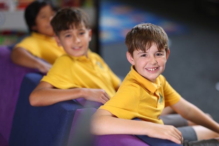 Three smiling boy students sitting in class and turning towards the camera.